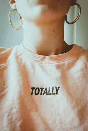 穿著蜜桃色衛衣印有「TOTALLY」字樣，戴著金色圓環耳環的人。