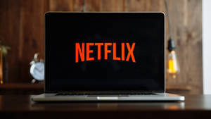 手提電腦在木桌上顯示Netflix標誌，配有復古時鐘和發光燈泡。 — Netflix GIF 壁紙