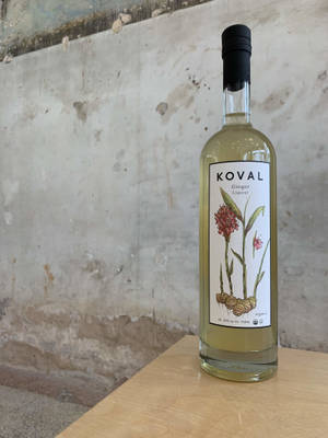 一瓶Koval Ginger Liqueur放在木頭上，背景是混凝土牆。