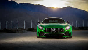 綠色 Mercedes-AMG GT 跑車停在沙漠中，背景有風力發電機和山脈，夕陽西下。