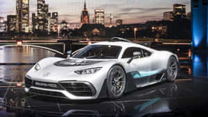 銀色 Mercedes-AMG 跑車在反射舞台上，背景是黃昏時分的城市天際線。