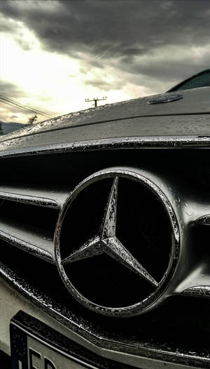 在暴風雨天空下，帶有雨滴的 Mercedes-Benz 汽車鬼面罩特寫。