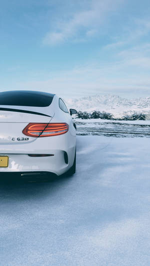 白色Mercedes C63停泊在雪地山景中，晴朗藍天下。