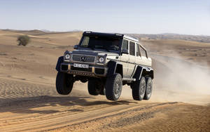 銀色梅賽德斯 G63 AMG 6x6 在沙漠中跳過沙丘。