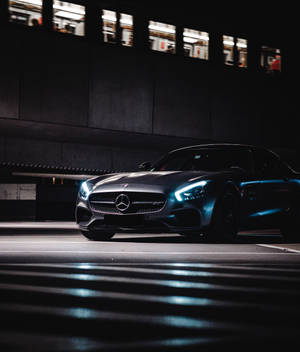 一輛黑色梅賽德斯-AMG GT在夜晚停放在天橋下，車頭燈在濕漉漉的路面上閃爍。