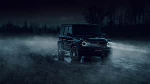黑色梅賽德斯-AMG G-Wagen在夜間穿過泥濘地形，車頭燈閃閃發光。