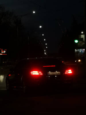 一輛汽車的紅色尾燈在路燈下的潮濕城市街道上夜間發光。