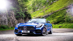 藍色 Mercedes-AMG GT 跑車在蜿蜒的山路上，周圍有綠色山丘。