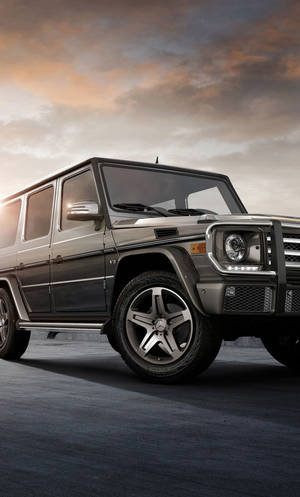 深灰色梅賽德斯 G-Class SUV 在帶有橙色和灰色雲彩的日落天空下。
