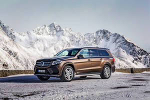 青銅色 Mercedes SUV 停泊在積雪道路上，背景有雪山。 — 汽車 壁紙
