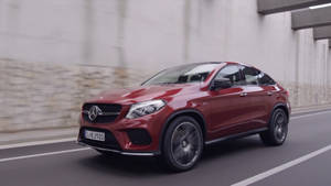 紅色梅賽德斯 GLE Coupe 在帶有模糊混凝土牆壁的城市道路上行駛。 — 汽車 壁紙