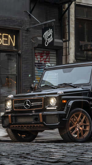 黑色Mercedes G-Wagen配金色輪圈夜間停泊在鵝卵石街道上。