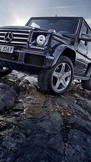 黑色 Mercedes G-Class SUV 在黃昏時分行駛於岩石地形。