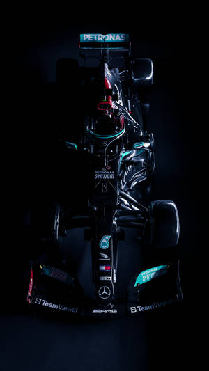 一架帶有Petronas品牌標誌的黑色和藍綠色一級方程式賽車，在昏暗的攝影棚中打光。