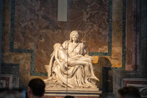 大理石 Pietà 雕塑，瑪利亞懷抱耶穌，在博物館展出，下方有遊客。