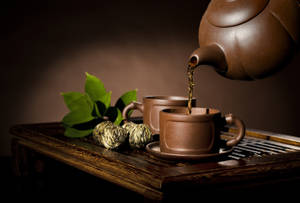 深色茶從陶壺倒入杯中，旁邊有綠葉和茶球。