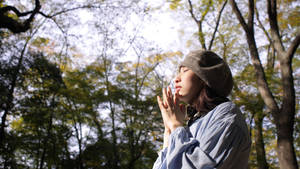 戴冷帽的年輕女性在秋樹下冥想，陽光穿過樹葉灑落。