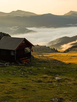 一座木造山間小屋在日出時俯瞰著充滿霧氣的山谷。 — 森林 壁紙