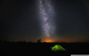 一個發光的綠色帳篷在星空夜空中，銀河在山脈之上。