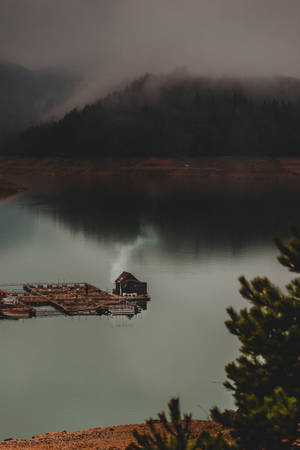浮動碼頭上的一座小屋在平靜的湖面上冒煙，周圍是霧氣繚繞的山巒。