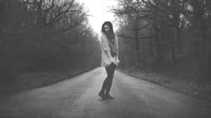 一位女性獨自站在森林道路上，在黑白畫面中顯得沮喪。 — 灰色 GIF 壁紙
