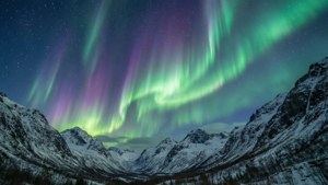 星空下，積雪的山峰上綠色和紫色的極光