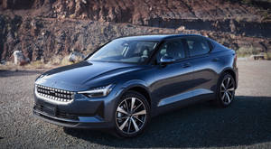 深灰色Polestar 2電動車停在碎石上，靠近紅色岩壁。 — 汽車 壁紙
