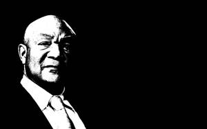 一個穿著西裝打領帶的光頭男人，在高對比度的黑白肖像中表情嚴肅。