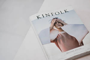 一本 KINFOLK 雜誌，女性遮住眼睛，放在白色表面上。 — 極簡美學 壁紙