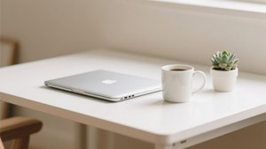 一部銀色手提電腦、一個咖啡杯和一小盆多肉植物在白色桌子上