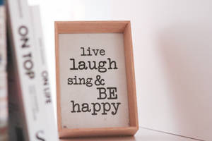 木框勵志語錄標牌，寫著 live laugh sing & BE happy，旁邊有書本。