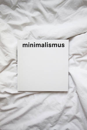 白色書本上印有 minimalismus 文字，放在皺巴巴的白色床單上