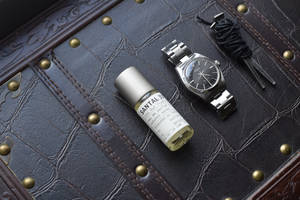 銀色手錶和 Santal 33 香水瓶放在帶黃銅鉚釘的深色皮革上。 — 極簡美學 壁紙