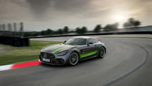 灰色Mercedes-AMG GT帶有綠色條紋，在日落時分的賽道上比賽。 — 汽車 壁紙