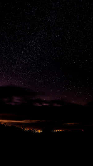 繁星點點的夜空，紫色雲彩和橙色地平線光芒籠罩著黑暗的樹木。