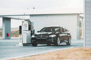 黑色BMW旅行車在現代化加油站，天空多雲。