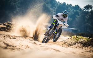 越野電單車手在沙地地形上高速行駛，揚起塵土。