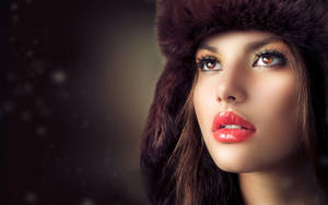 戴皮草帽、紅唇的女性在雪景中向上看。