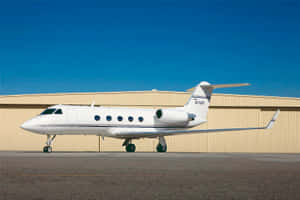 白色私人飛機停在機庫前停機坪上，藍天白雲
