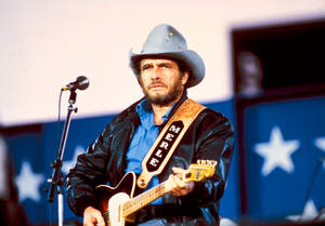Merle Haggard 在星空背景的舞台上彈結他。