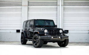 黑色Jeep Wrangler停泊在白色車庫門前的混凝土上。