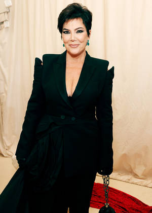 Kris Jenner 喺正式活動中身穿帶有荷葉邊肩部同鏈條手袋嘅黑色西裝外套。