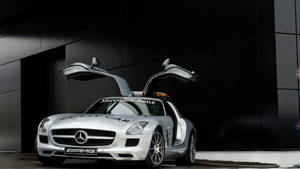銀色平治 SLS AMG 安全車，鷗翼車門打開，停在黑色建築前。