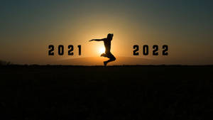 日落時分，一個人在2021年和2022年之間跳躍的剪影。
