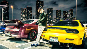 年輕男子在夜晚的城市停車場中靠在兩輛跑車之間。