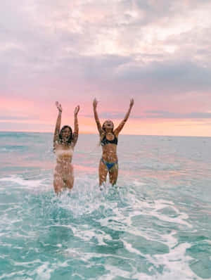 日落時分，兩位女性舉起雙臂跳入海水中