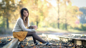 年輕女性坐在鐵軌上，日落時分被秋葉環繞。