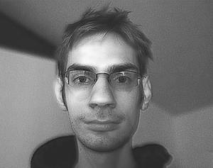 一個戴眼鏡嘅男人喺黑白肖像中直視鏡頭。