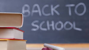 一堆書本和粉筆放在黑板前，黑板上寫着 back to school。