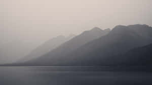 在朦朧的黎明天空下，霧氣籠罩的山峰映襯著寧靜的山間湖泊。